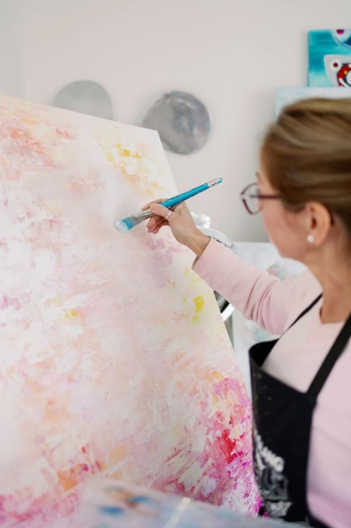 Close-up of Ritushka building a textured pink and gold abstract surface with a brush