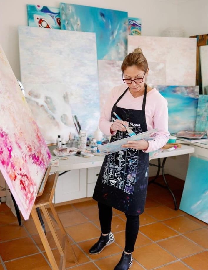 Ritushka mixing acrylic paint on a palette in front of a large abstract canvas